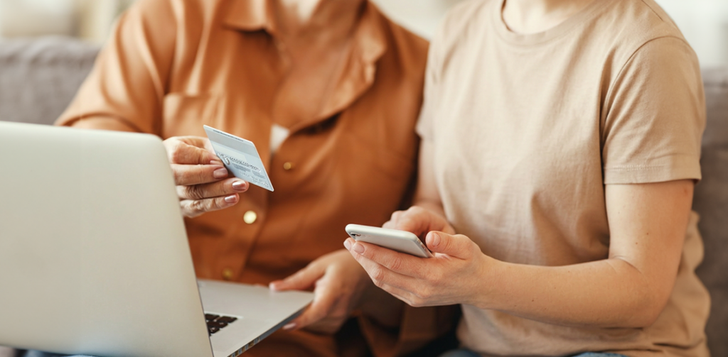 Duas mulheres usando celular e notebook enquanto se atentam à prevenção de fraudes e Machine Learning.