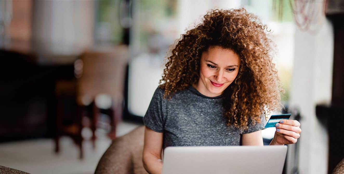 Imagem de uma mulher segurando um cartão de crédito e olhando para o computador