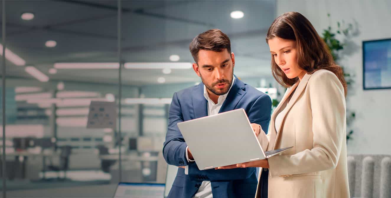 Homem e mulher em um ambiente corporativo com um notebook em mãos olhando para a tela